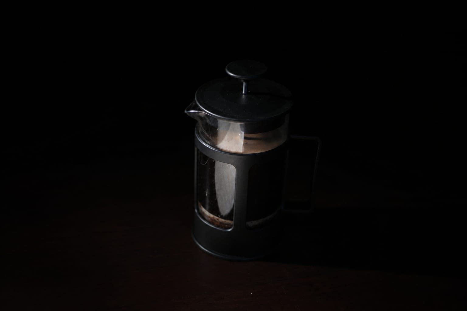 A French press holding freshly brewed coffee against a dark background.