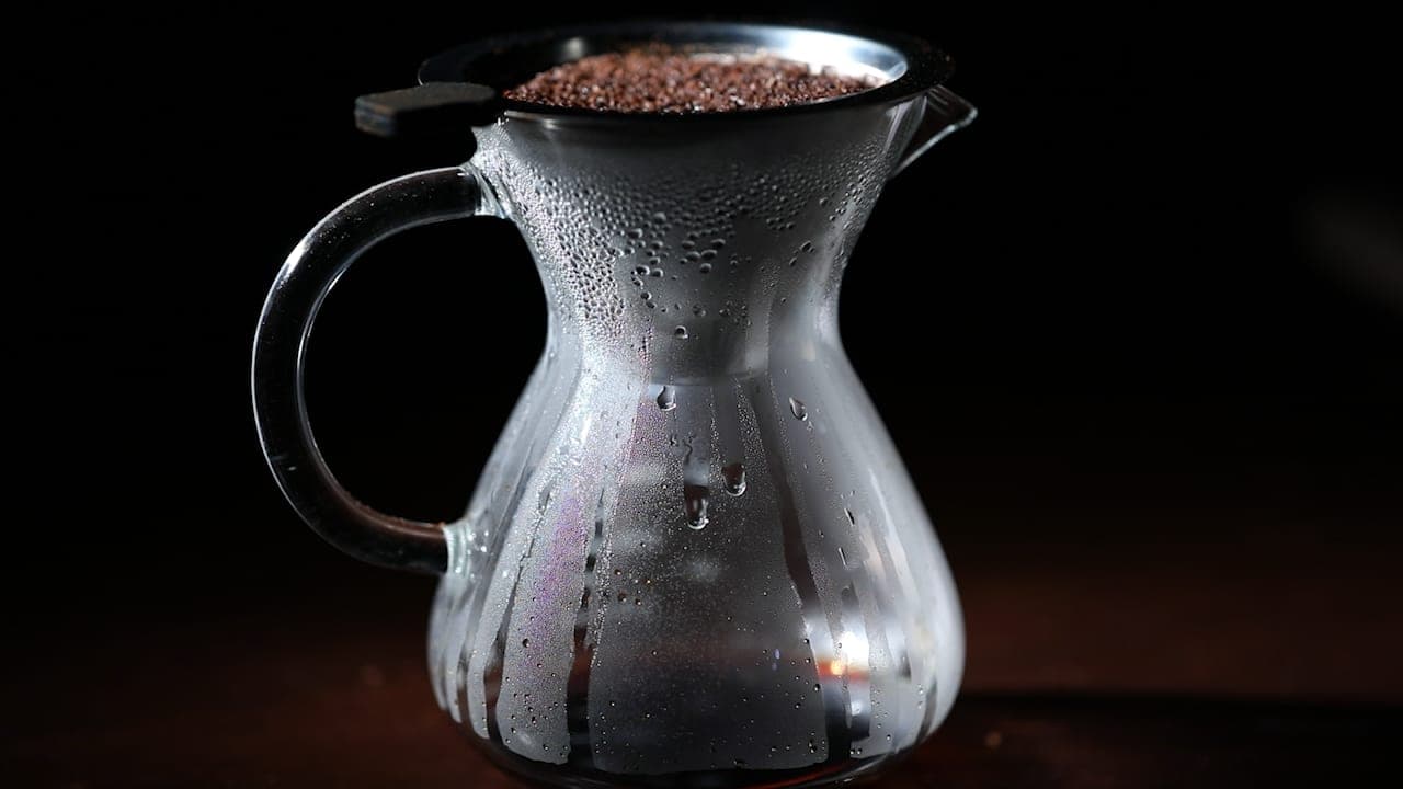A glass pour-over carafe, beaded with steam, against a dark background.