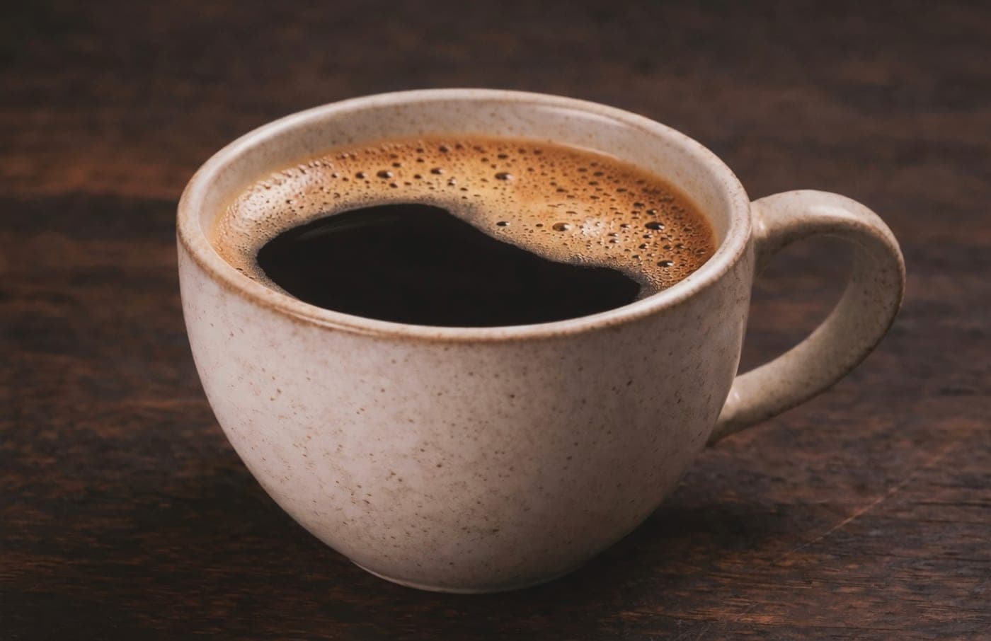 A ceramic cup of freshly brewed black coffee on a dark wooden table.